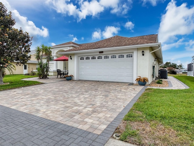 view of front of home featuring an attached garage, stucco siding, central AC unit, and a front yard
