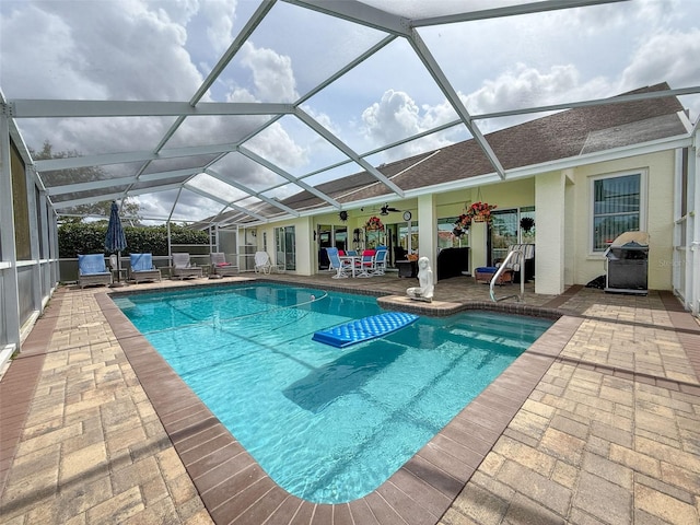 outdoor pool with a patio area, a ceiling fan, and glass enclosure