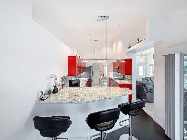 kitchen with a sink, a peninsula, stainless steel appliances, a breakfast bar, and hanging light fixtures