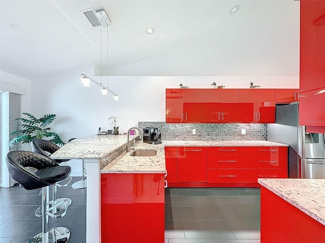 kitchen featuring a sink, a peninsula, stainless steel refrigerator with ice dispenser, decorative backsplash, and red cabinets