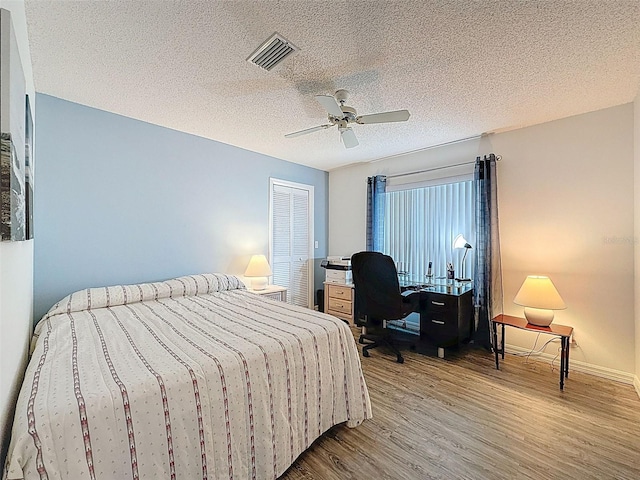 bedroom with a ceiling fan, a textured ceiling, baseboards, visible vents, and wood finished floors