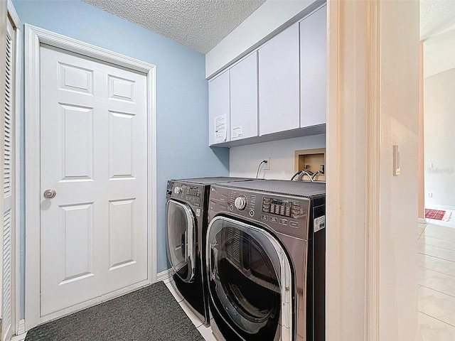 clothes washing area with washing machine and clothes dryer, a textured ceiling, and cabinet space