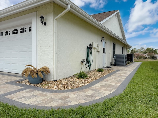 view of side of home featuring central air condition unit, an attached garage, stucco siding, and a yard