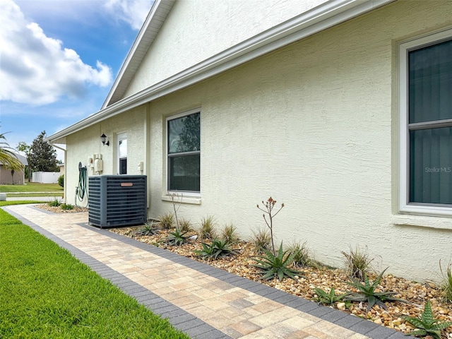 view of property exterior featuring a lawn, cooling unit, and stucco siding