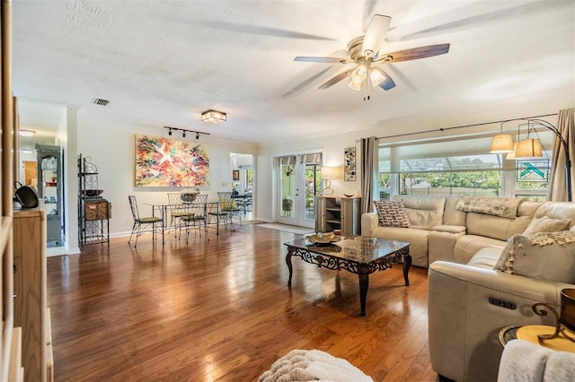 living room with ceiling fan, a textured ceiling, baseboards, wood finished floors, and visible vents