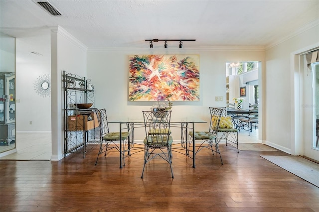 dining room with wood-type flooring, crown molding, visible vents, and rail lighting
