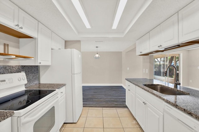 kitchen with white cabinets, a sink, white appliances, dark stone countertops, and a tray ceiling