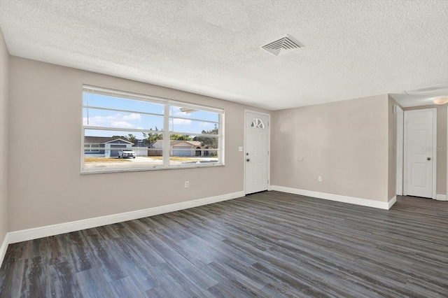 empty room with baseboards, a textured ceiling, dark wood finished floors, and visible vents