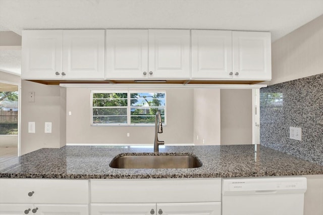kitchen with a sink, dark stone counters, dishwasher, and white cabinetry