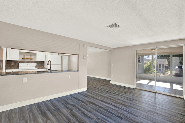 unfurnished living room featuring a textured ceiling, visible vents, a sink, baseboards, and dark wood-style floors
