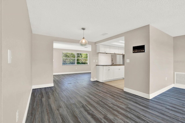 unfurnished living room featuring a textured ceiling, baseboards, visible vents, and wood finished floors