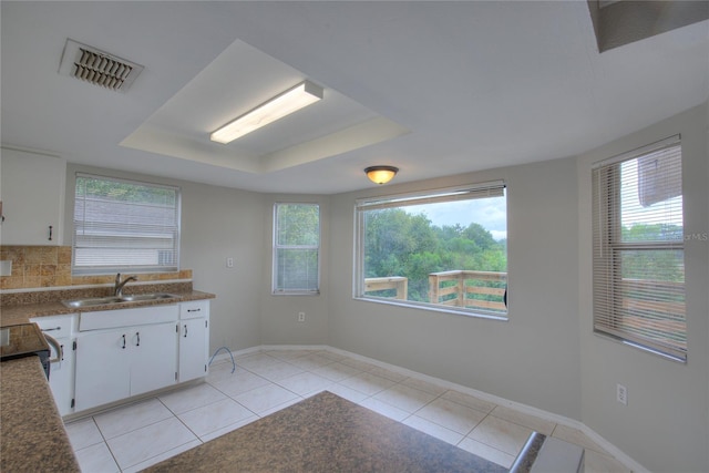 kitchen with white cabinets, a sink, light tile patterned floors, a tray ceiling, and visible vents