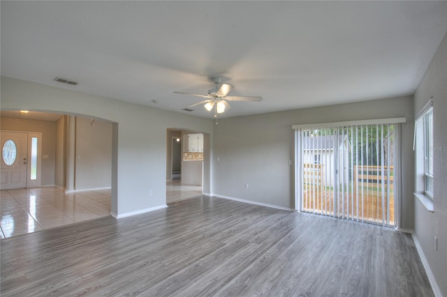unfurnished living room featuring arched walkways, ceiling fan, a wealth of natural light, and visible vents