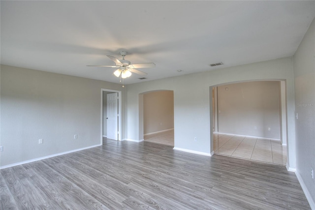 unfurnished room featuring visible vents, a ceiling fan, baseboards, arched walkways, and light wood-style flooring