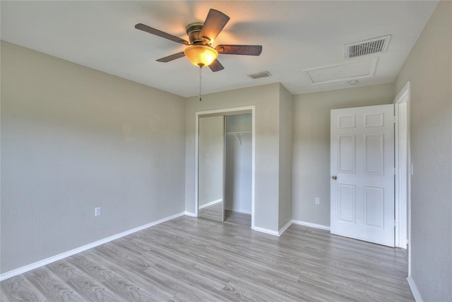 unfurnished bedroom with visible vents, attic access, light wood-style flooring, and a closet