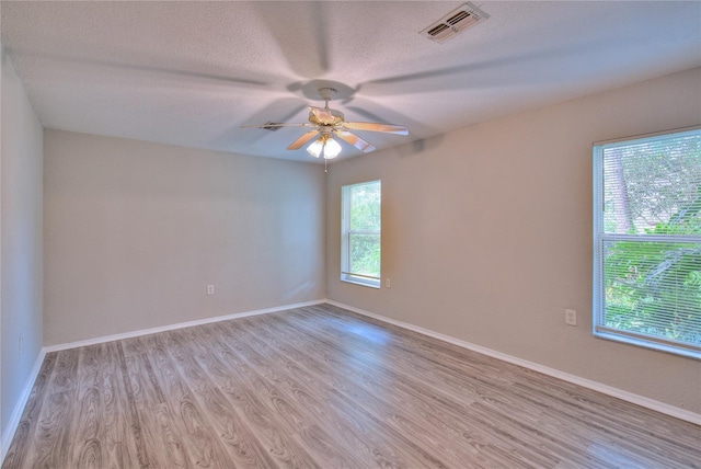 empty room featuring a ceiling fan, a textured ceiling, visible vents, wood finished floors, and baseboards