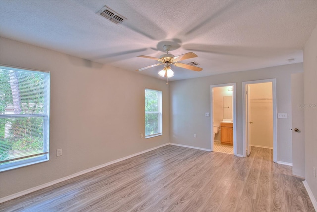 unfurnished bedroom with visible vents, light wood-style floors, baseboards, a walk in closet, and a textured ceiling