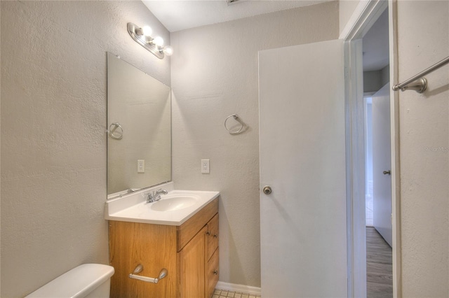 half bathroom featuring toilet, a textured wall, and vanity