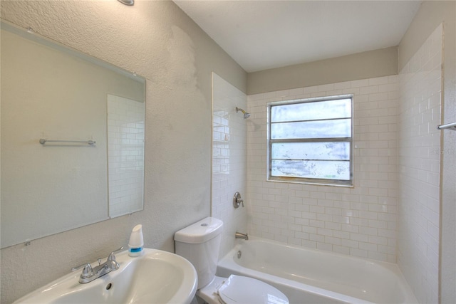 bathroom featuring toilet, a textured wall, a sink, and bathtub / shower combination