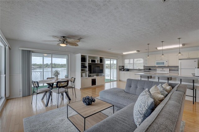 living room with a ceiling fan, a textured ceiling, wainscoting, and a wealth of natural light