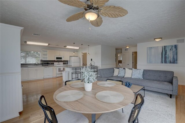 dining room featuring visible vents, a textured ceiling, light wood-style flooring, and a ceiling fan
