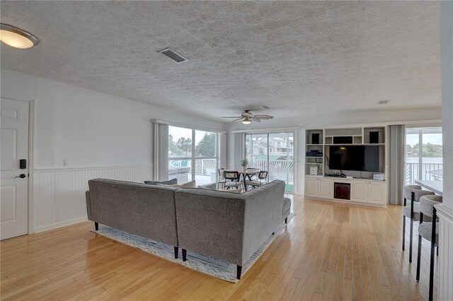 living area with light wood-type flooring, a ceiling fan, wainscoting, and visible vents