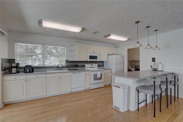 kitchen with open shelves, a peninsula, white appliances, a breakfast bar area, and independent washer and dryer