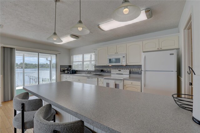 kitchen with a textured ceiling, hanging light fixtures, white cabinets, a breakfast bar, and white appliances