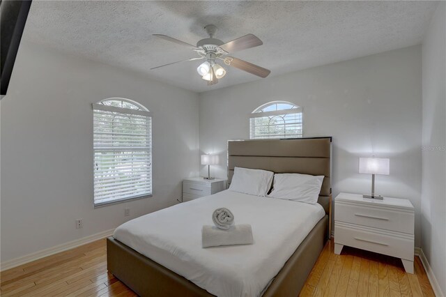 bedroom with a textured ceiling, baseboards, ceiling fan, and light wood-style flooring