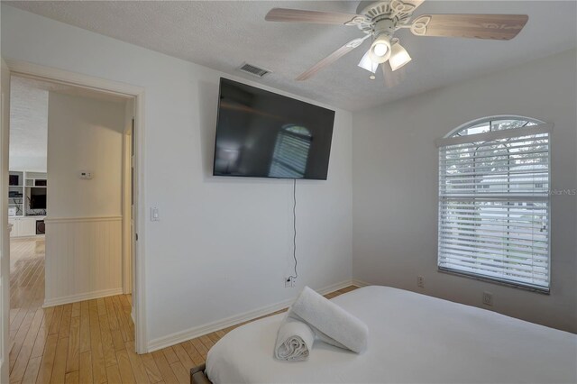 bedroom with visible vents, wainscoting, light wood-style floors, baseboards, and a ceiling fan