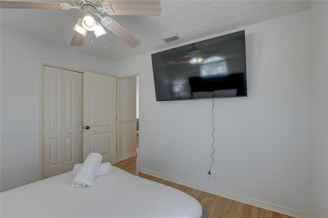 bedroom with visible vents, a closet, wood finished floors, baseboards, and ceiling fan