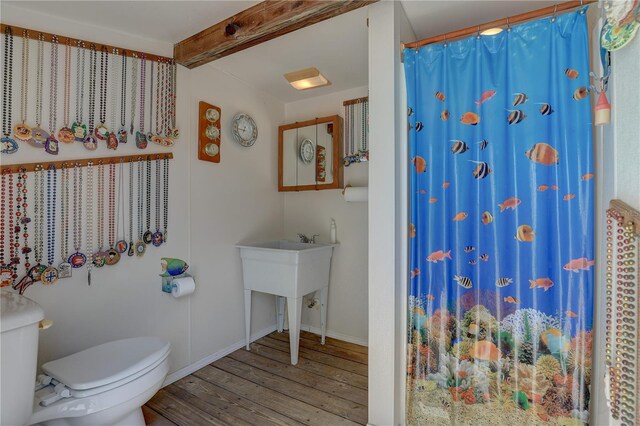 bathroom with toilet, a shower with shower curtain, baseboards, wood finished floors, and beamed ceiling