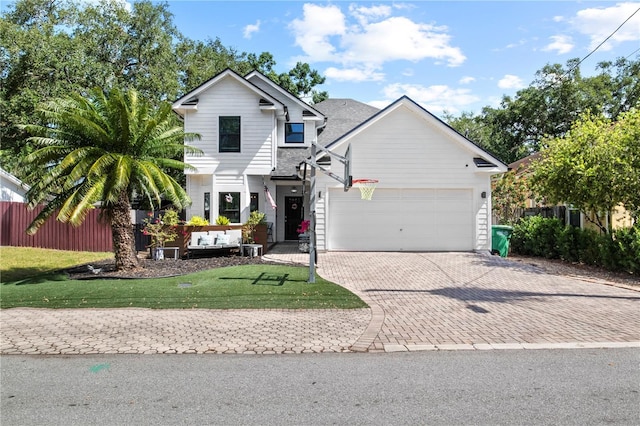 traditional-style house with an attached garage, decorative driveway, fence, and a front yard