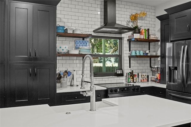 kitchen with open shelves, wall chimney range hood, light countertops, stainless steel fridge with ice dispenser, and backsplash