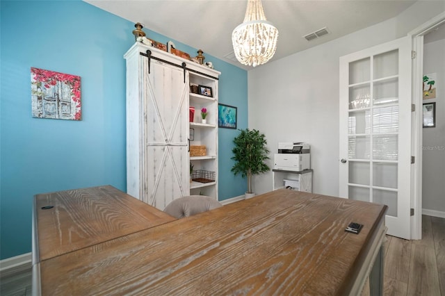 office space featuring a barn door, baseboards, an inviting chandelier, visible vents, and wood finished floors