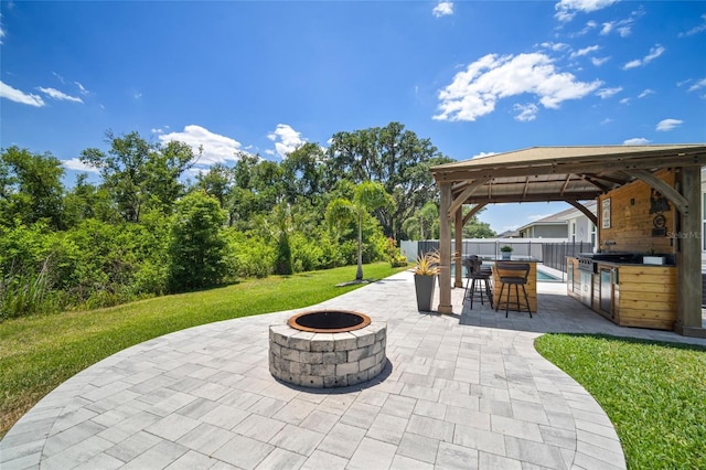 view of patio featuring a fire pit, fence, outdoor dry bar, a gazebo, and an outdoor kitchen