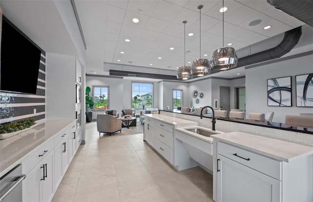 kitchen with open floor plan, white cabinetry, a tray ceiling, light stone counters, and a sink