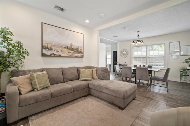 living area with baseboards, visible vents, wood finished floors, and a notable chandelier
