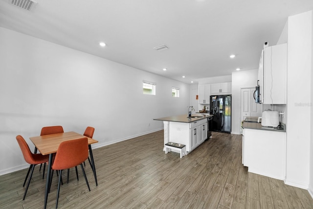 11819 Brighton Knoll Loop, Riverview, FL 33579 - kitchen featuring black refrigerator with ice dispenser, a sink, dark countertops, wood finished floors, and a center island with sink