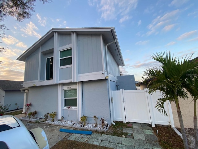 property exterior at dusk featuring fence, a gate, and stucco siding