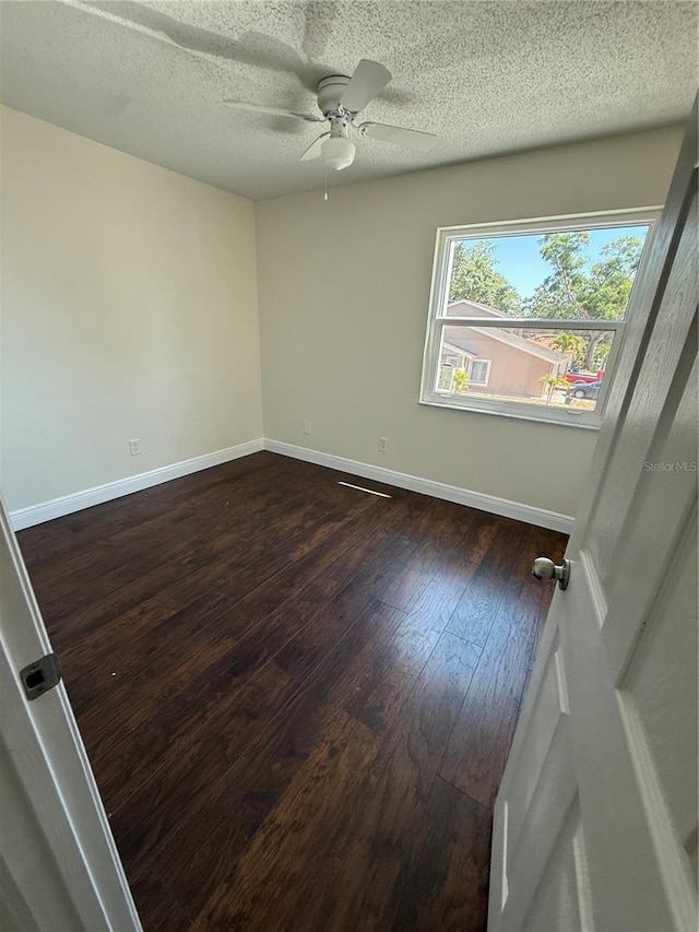 spare room featuring baseboards, a ceiling fan, a textured ceiling, and dark wood-type flooring