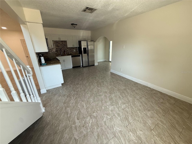 unfurnished living room featuring visible vents, a sink, baseboards, a textured ceiling, and arched walkways
