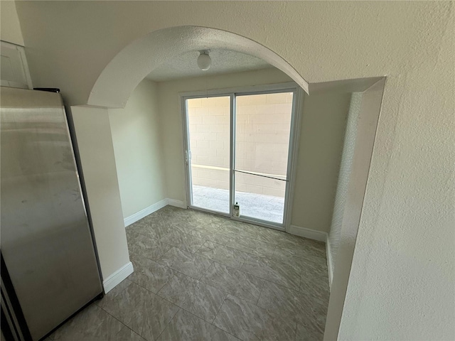 unfurnished room with arched walkways and baseboards