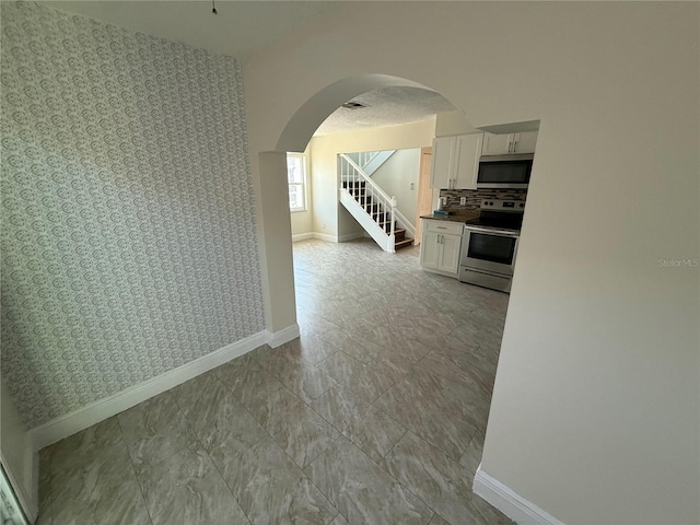 spare room featuring stairs, arched walkways, baseboards, and wallpapered walls