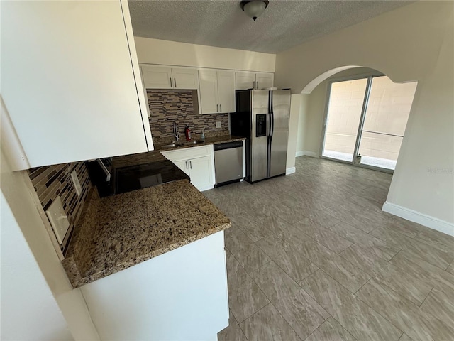 kitchen with white cabinetry, arched walkways, appliances with stainless steel finishes, and tasteful backsplash