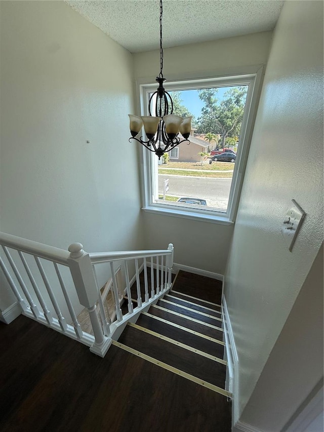 staircase with baseboards, a textured ceiling, wood finished floors, and a chandelier