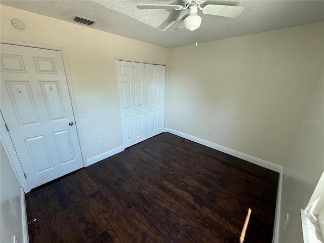unfurnished bedroom featuring visible vents, a closet, baseboards, a textured ceiling, and dark wood finished floors