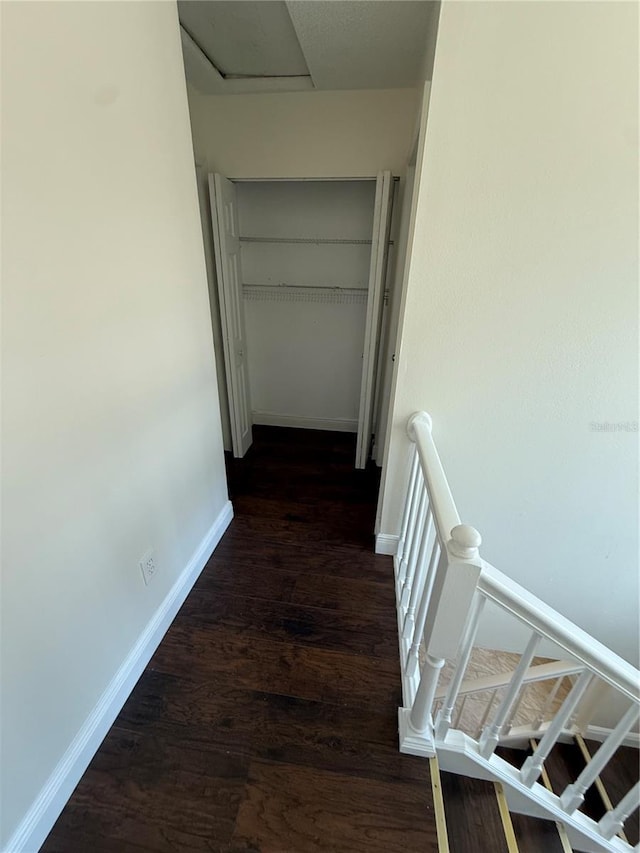 hallway featuring baseboards, wood finished floors, and an upstairs landing
