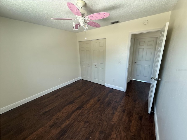 unfurnished bedroom with dark wood-type flooring, a textured ceiling, baseboards, and a closet