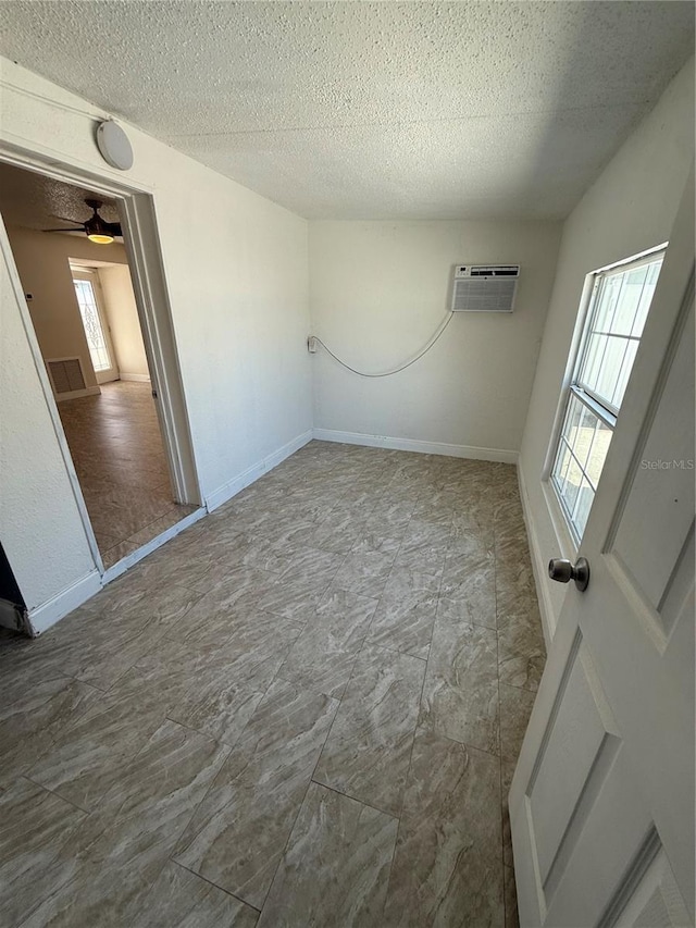 unfurnished room with a textured ceiling, visible vents, baseboards, and a wall mounted air conditioner